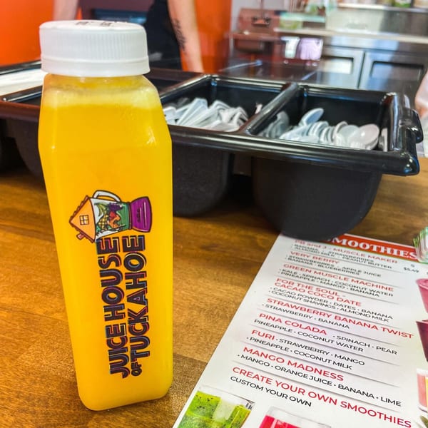 A bottle of yellow Juice House of Tuckahoe juice sits next to a smoothie menu.