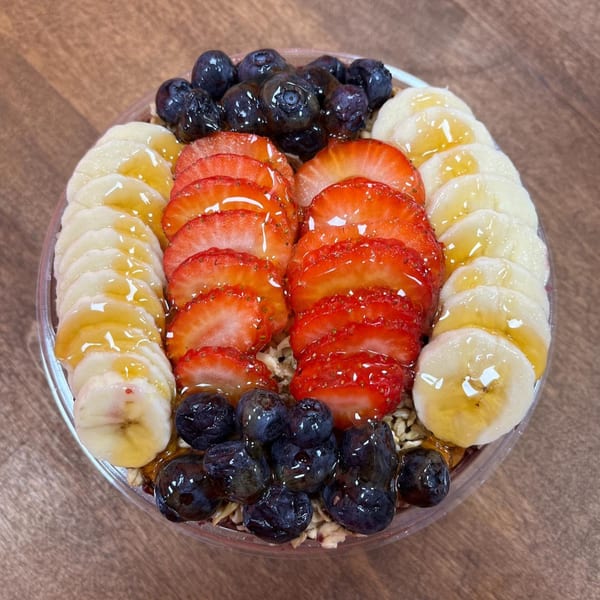 A colorful Juice House of Tuckahoe acai bowl with sliced bananas, strawberries, and blueberries drizzled with honey.