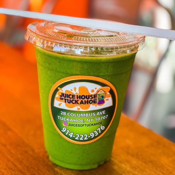 Green smoothie in a clear cup with a Juice House of Tuckahoe label and a straw.