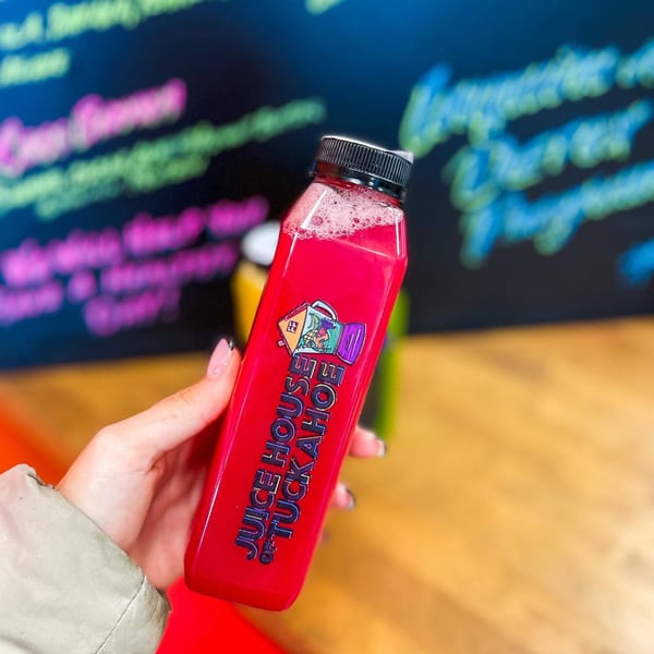 Hand holding a vibrant red Juice House of Tuckahoe bottle with a colorful logo.
