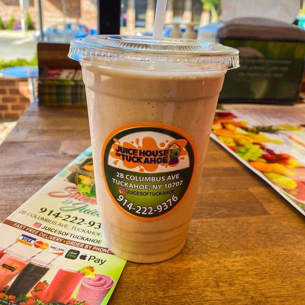 A Juice House of Tuckahoe smoothie with a straw on a wooden table with a menu.
