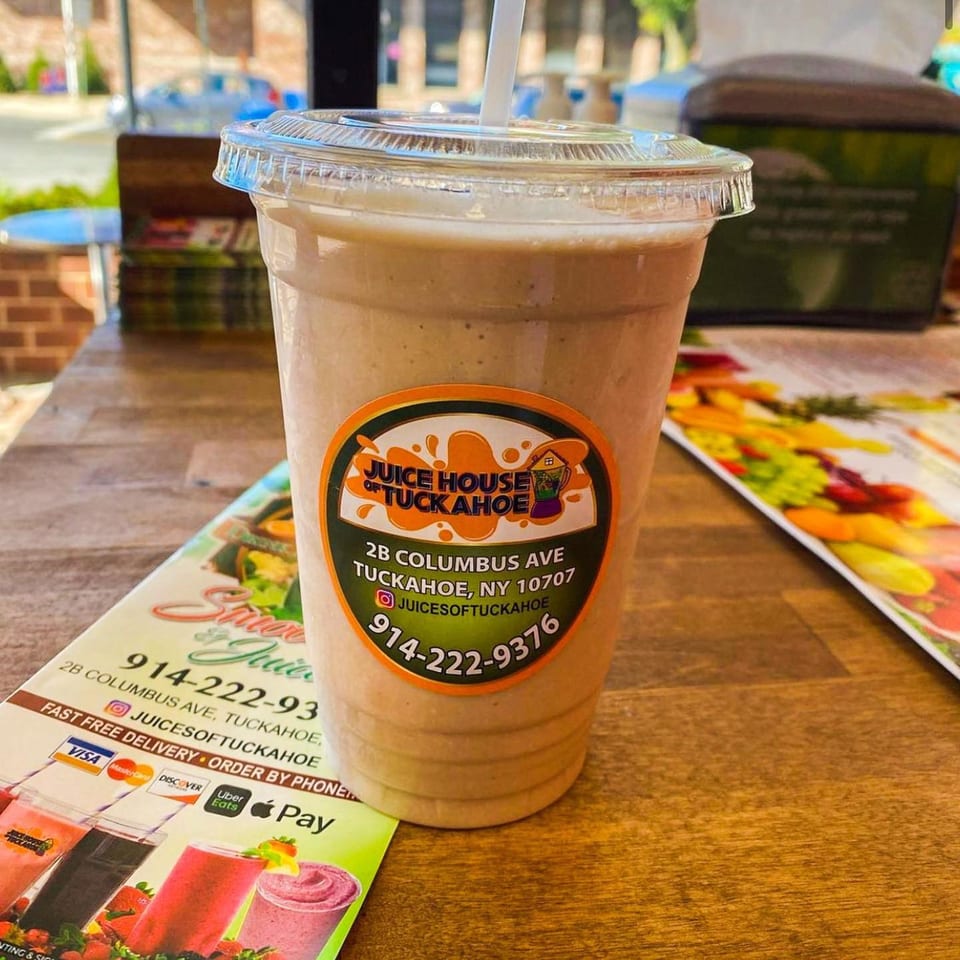 A Juice House of Tuckahoe smoothie with a straw on a wooden table with a menu.