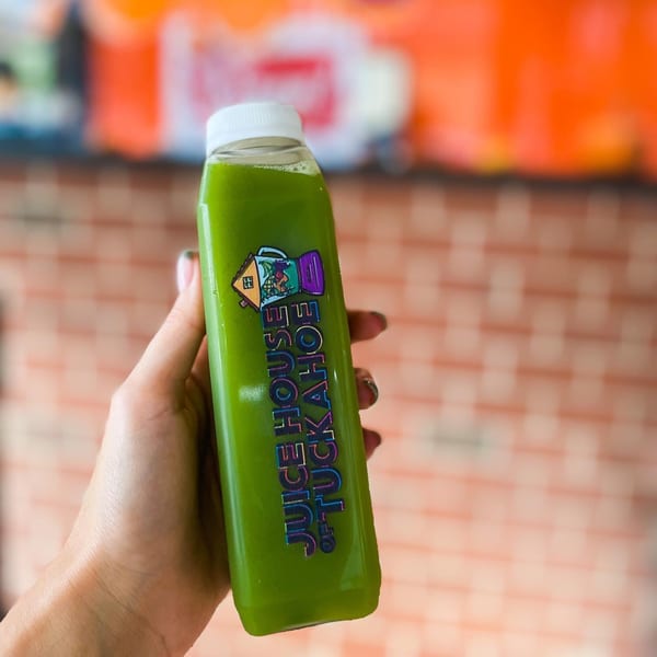 Hand holding a bottle of green juice with the "Juice House of Tuckahoe" logo.